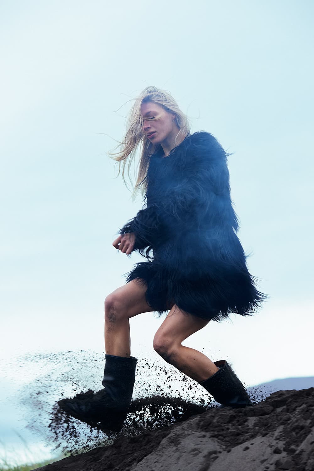 Woman in a black fur coat kicking up black sand