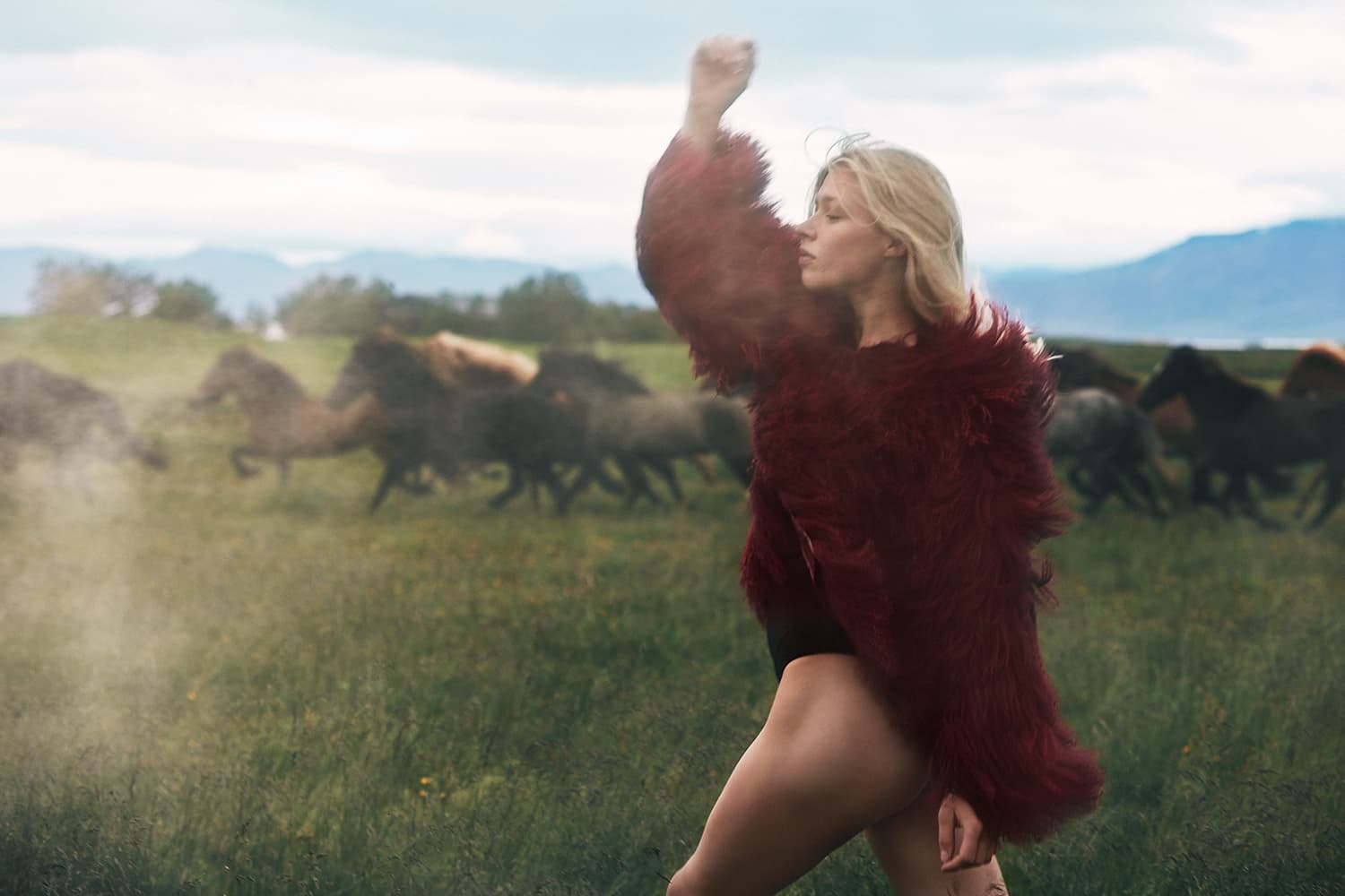 Woman in a red fur coat running ahead of wild horses