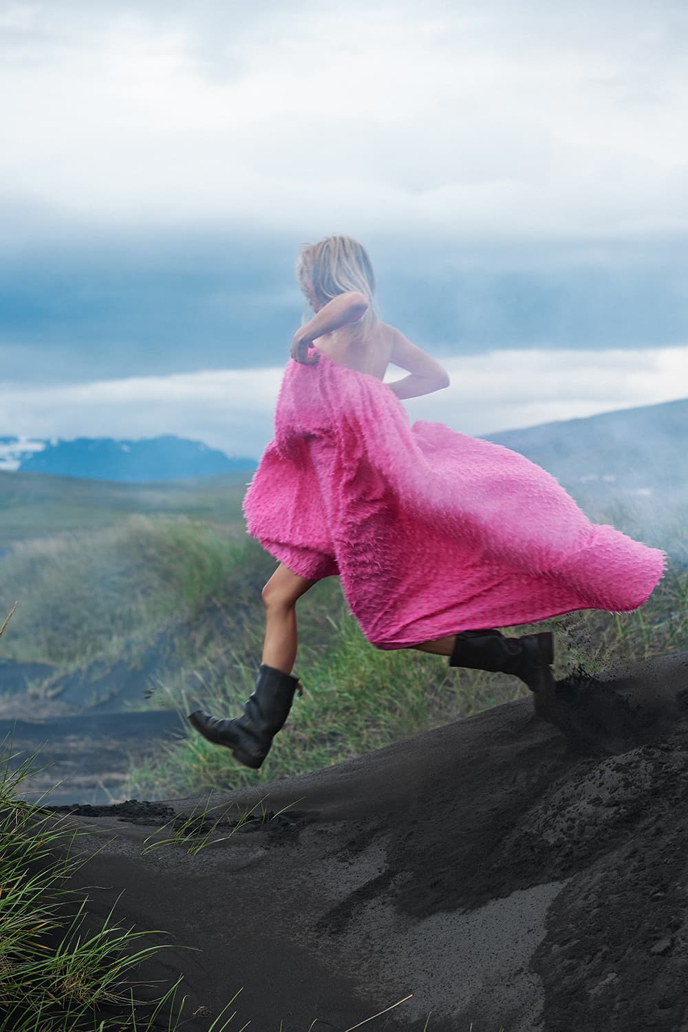 Woman in a pink dress striding over black volcanic sand
