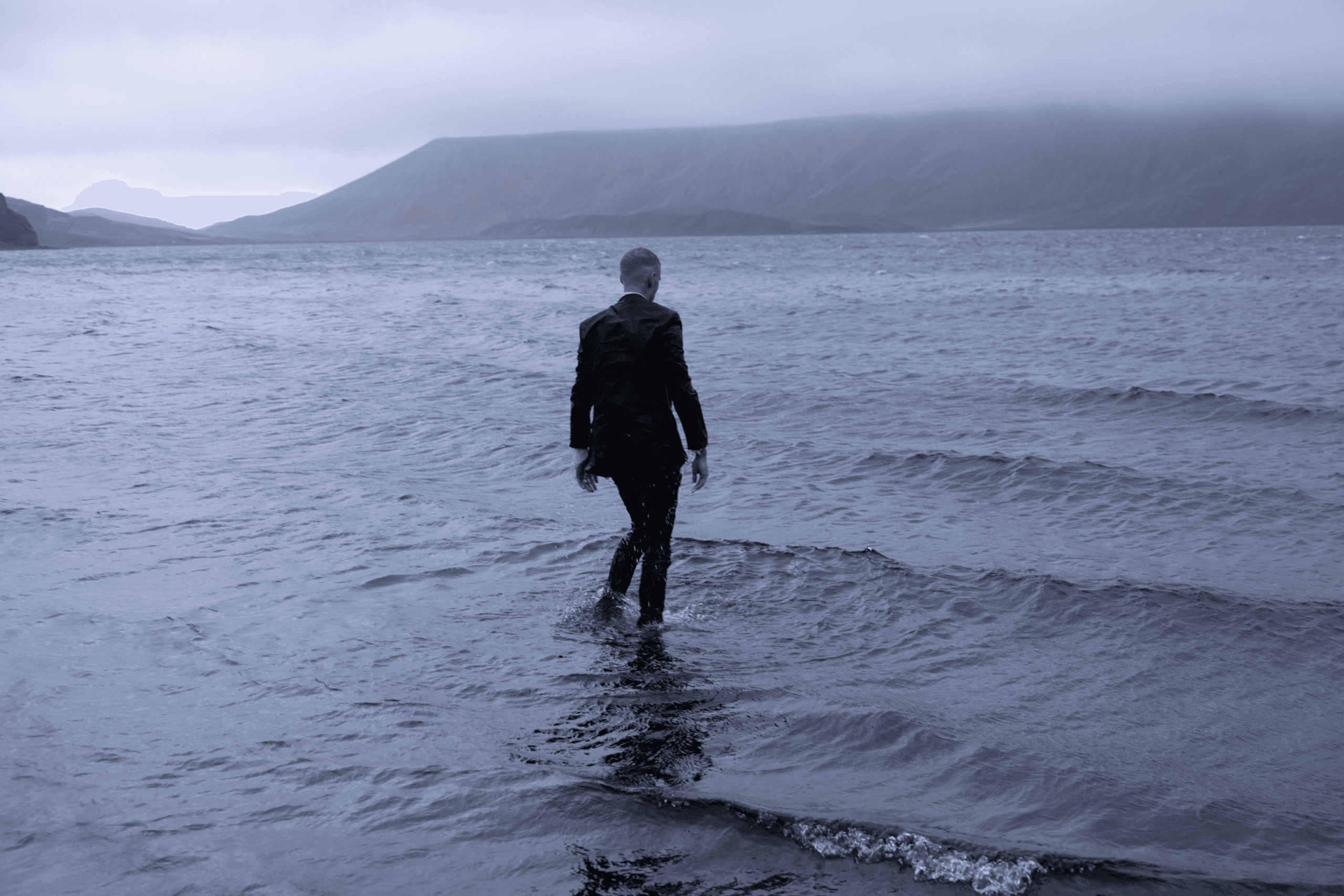 Man in a black suit wading into a lake